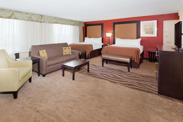 Habitación de hotel con dos camas, un sofá, una silla, un escritorio y un televisor.