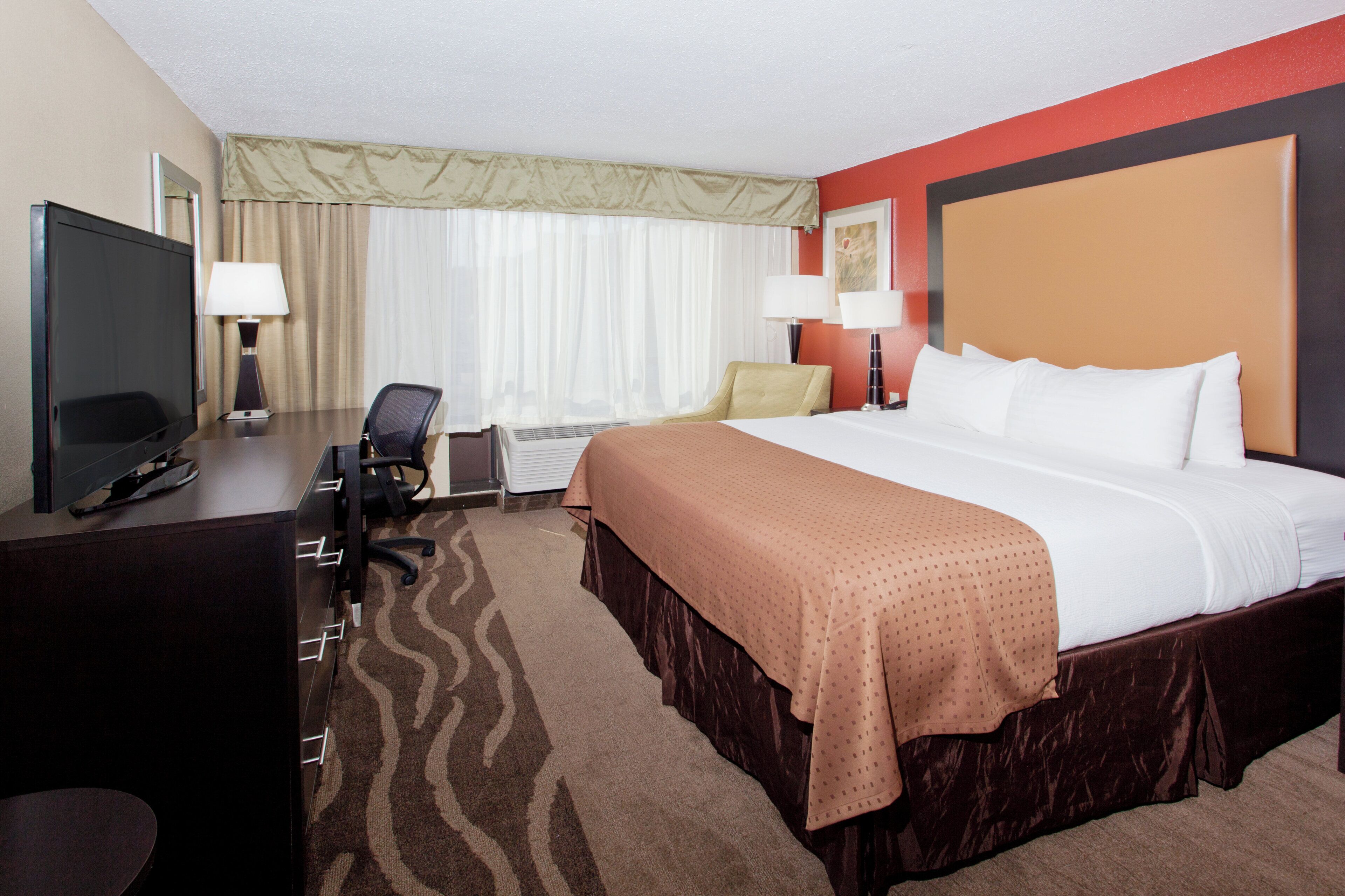 A hotel room with a bed, desk, chair, television, and a window with curtains.