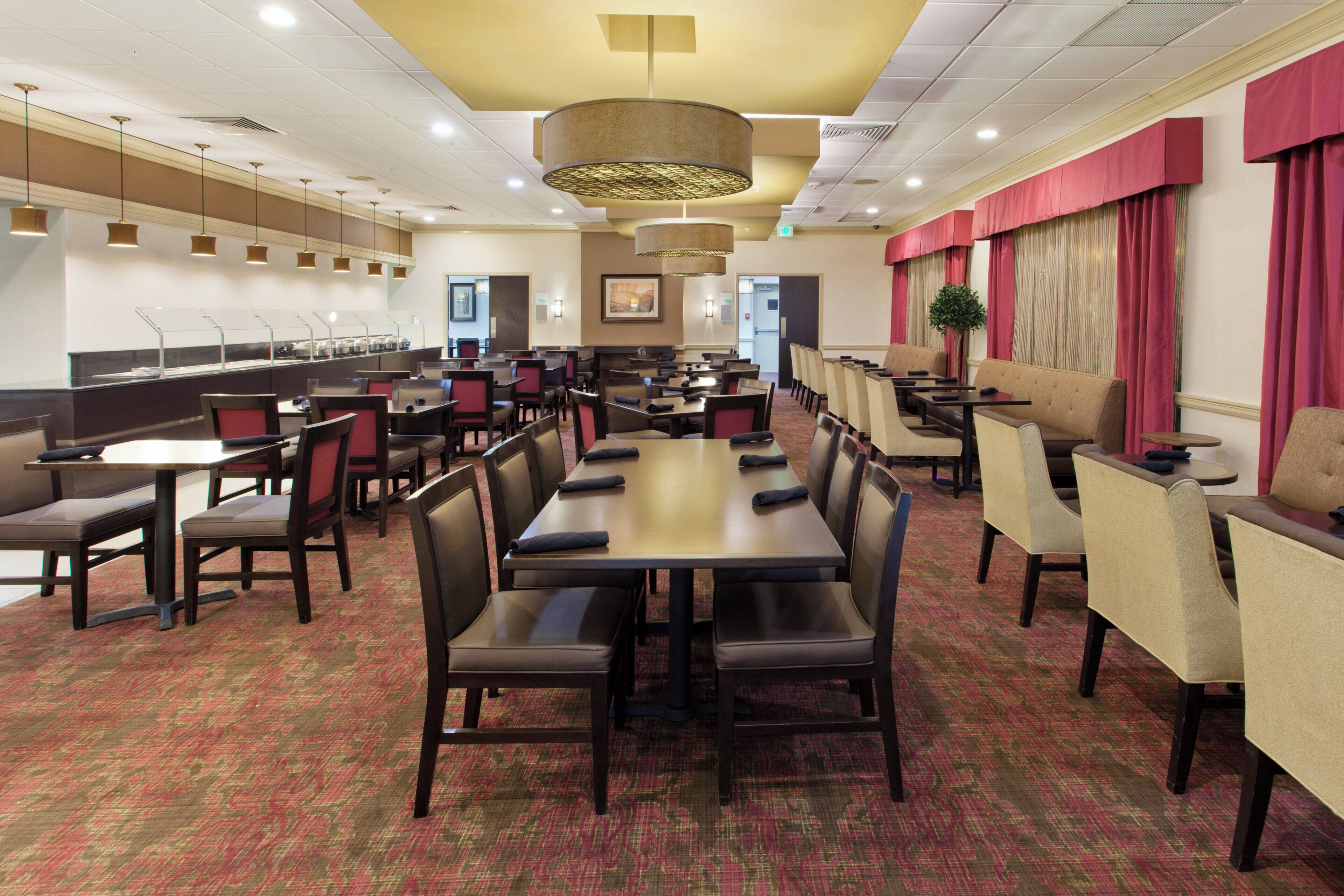 Ein Speisesaal eines Hotels mit mehreren Tischen, Stühlen, einer Buffettheke und einer großen Chandelier.