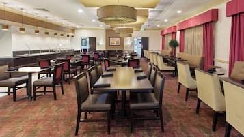 Ein Speisesaal eines Hotels mit mehreren Tischen, Stühlen, einer Buffettheke und einer großen Chandelier.