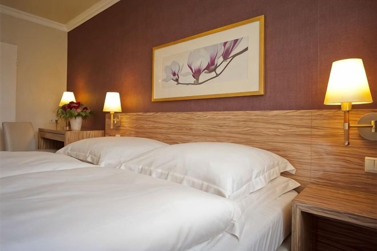 A hotel room with a large bed, two bedside lamps, a framed artwork on the wall, and a nightstand with a lamp.