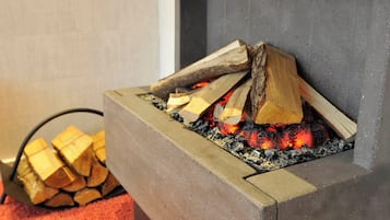 Een haardvuur met brandende blokken hout en een stapelhout ernaast.