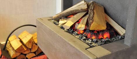Chimenea con leña ardiendo y un montón de leña a un lado.