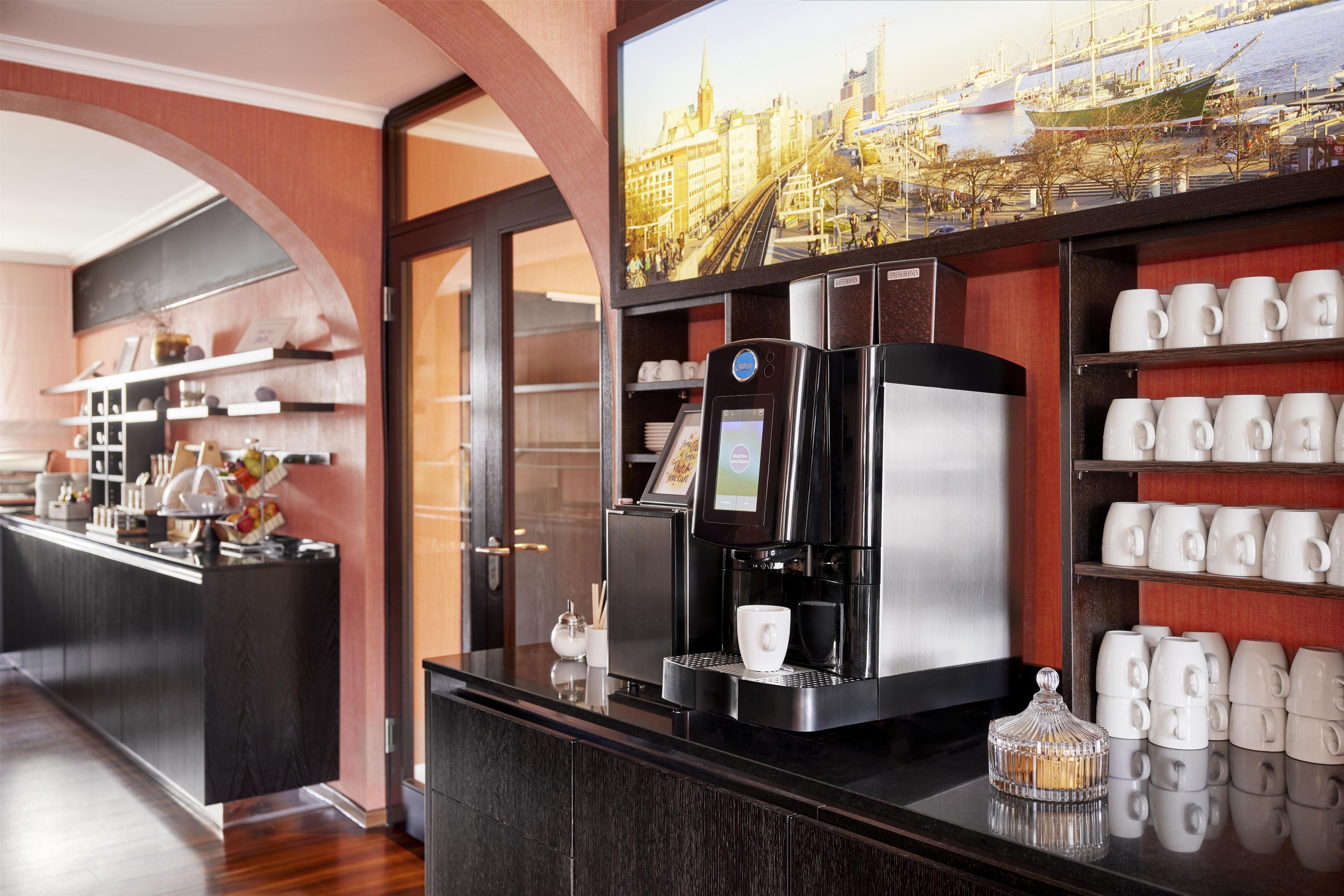Una hall d'hotel moderna con una macchina per caffè, vista sulla città ed esposizione di tazze.