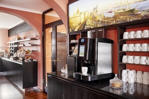 A modern hotel lobby with a coffee machine, a cityscape view, and a display of mugs. - Best Western Raphael Hotel Altona (Hamburg)