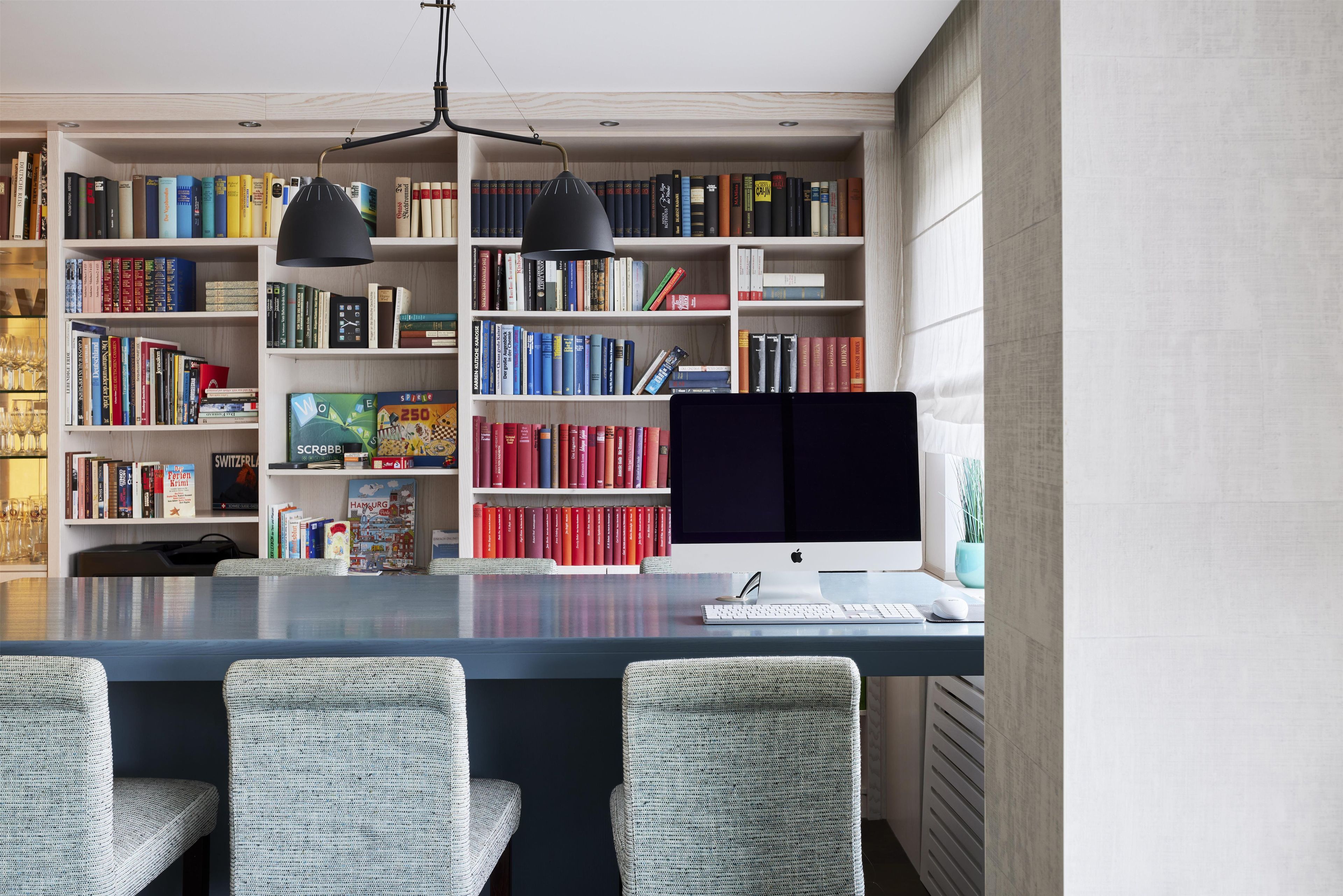 Une bibliothèque moderne dotée d’une vaste collection de rayonnages, d’un bureau avec un ordinateur et de trois fauteuils en osier.