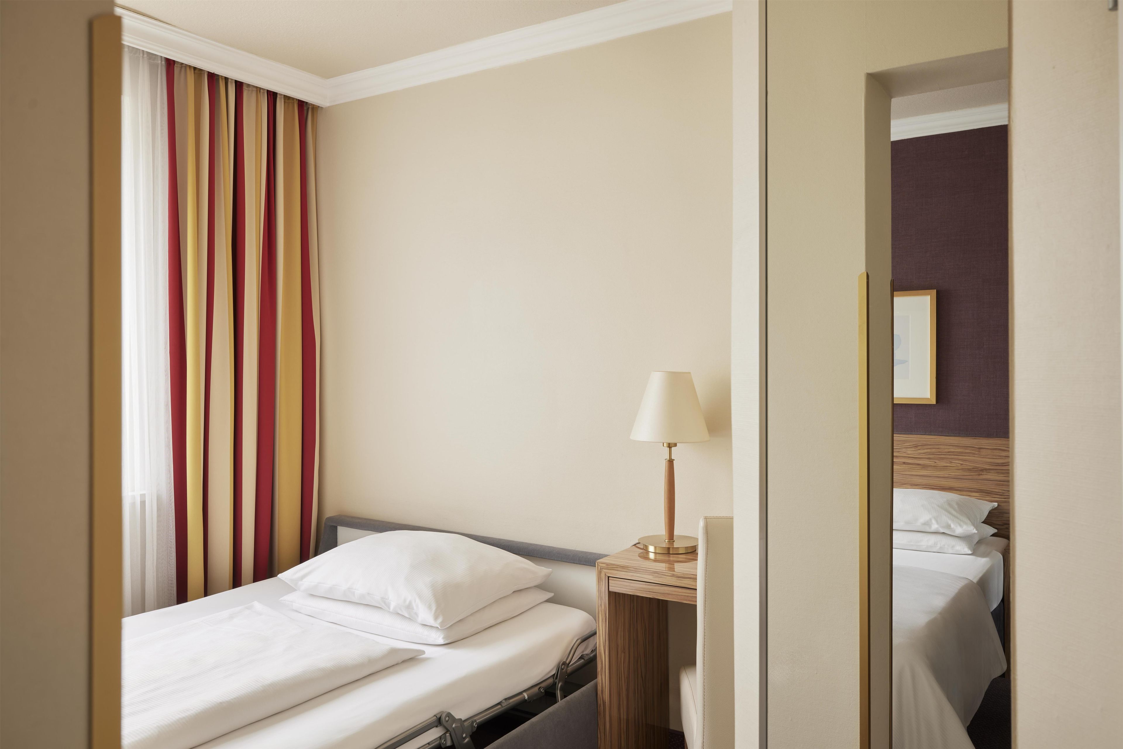 A hotel room with a single bed, a bedside table with a lamp, and a window with curtains.