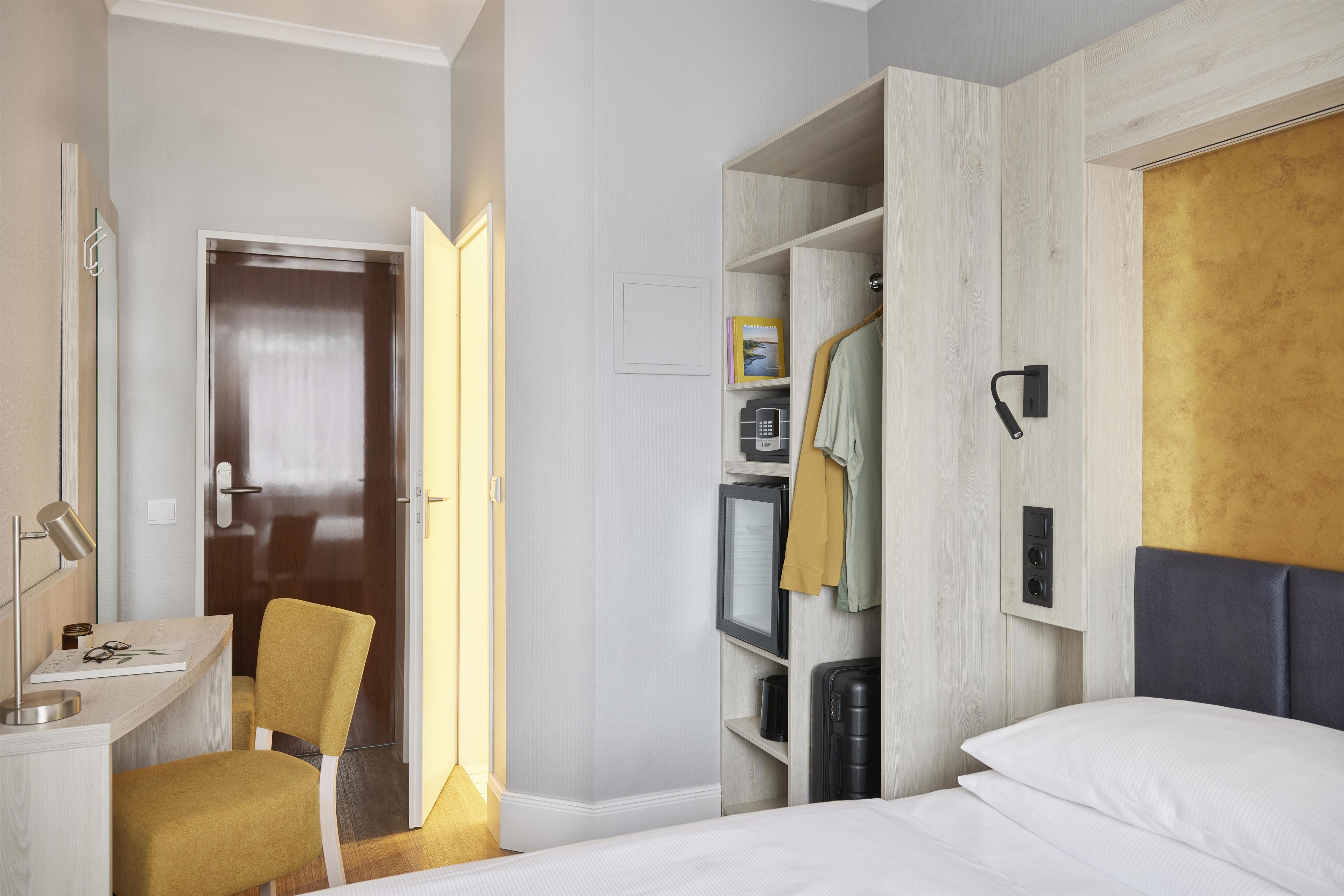 A hotel room with a bed, a desk, a chair, a wardrobe, and a mirror.