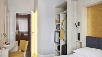 A hotel room with a bed, a desk, a chair, a wardrobe, and a mirror.