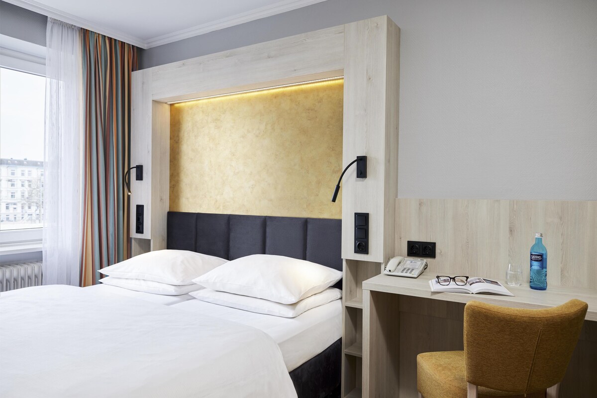 A hotel room with a bed, a desk with a chair, a telephone, and a bottle of water.