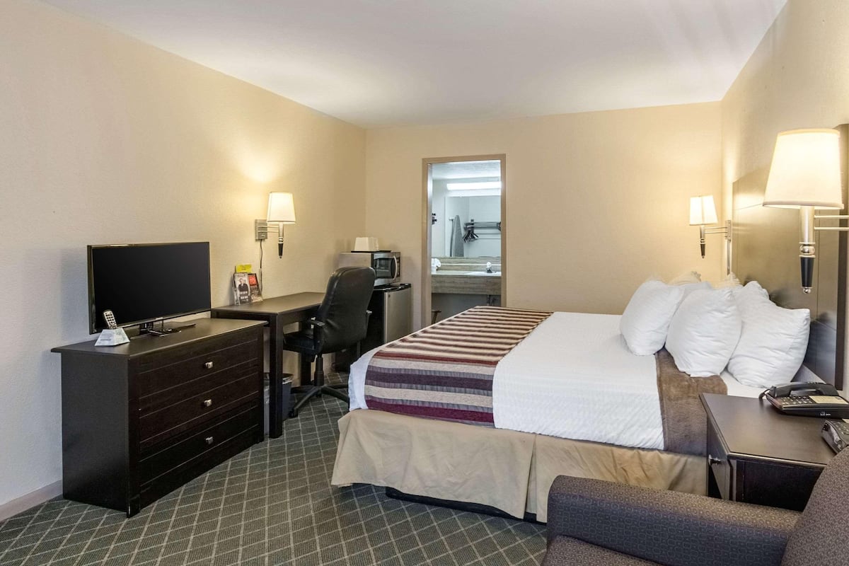 A hotel room with a bed, a desk with a computer, a TV, a dresser, and a mirror.