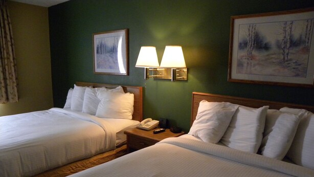 Habitación de hotel con dos camas, una mesita de noche con lámpara y dos cuadros en la pared.