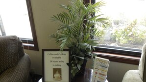 Letrero enmarcado que indica que hay café y galletas disponibles las 24 horas en la recepción, una planta en maceta y un menú sobre una mesa.