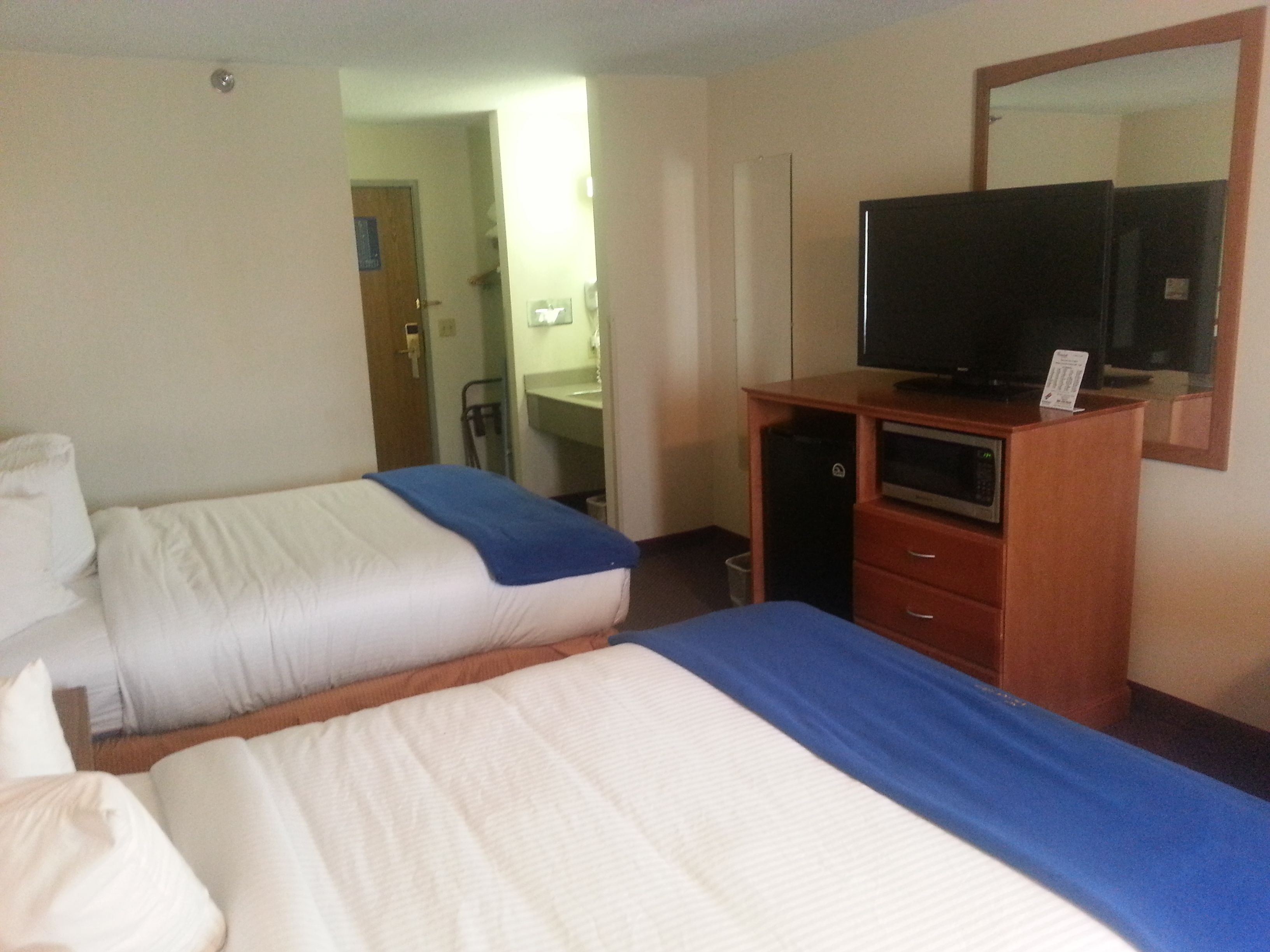 A hotel room with two beds, a television on a wooden dresser, and a bathroom visible through an open door.