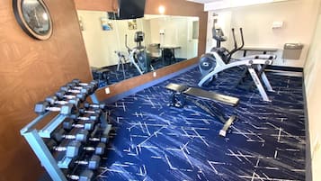 Une salle de sport équipée de matériel d’exercice, notamment des haltères, un banc et des appareils de cardio.