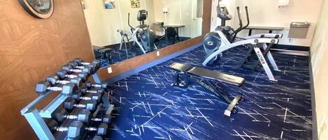 Un gimnasio con equipo de ejercicio, incluyendo mancuernas, un banco y máquinas de cardio.