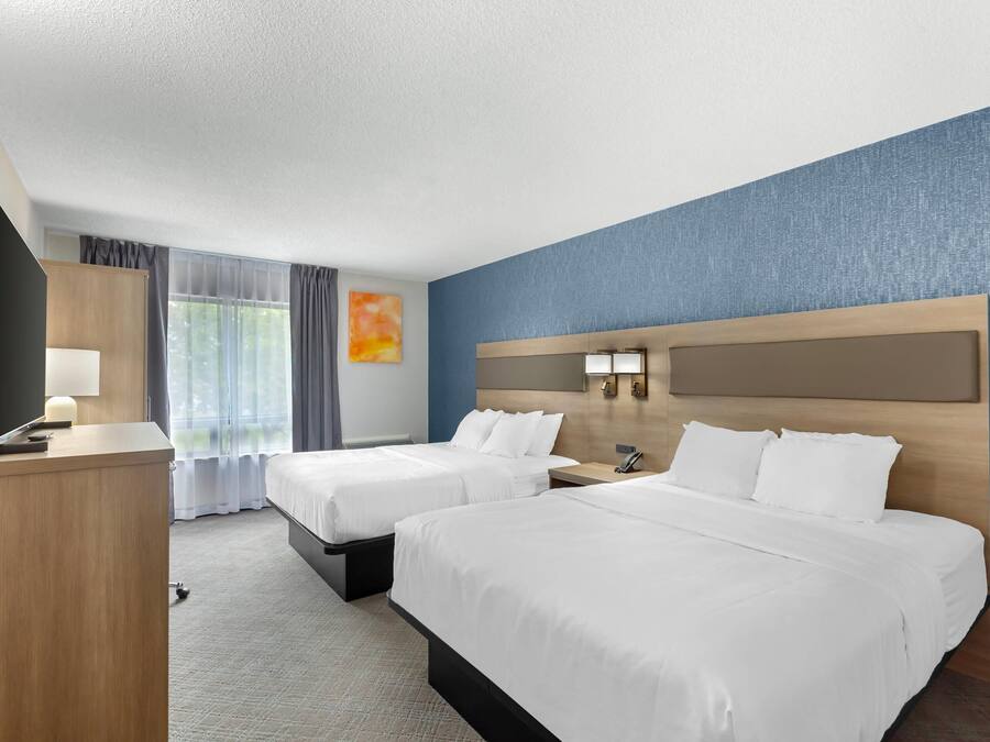 Habitación de hotel con dos camas, un escritorio, un televisor y una ventana con cortinas.