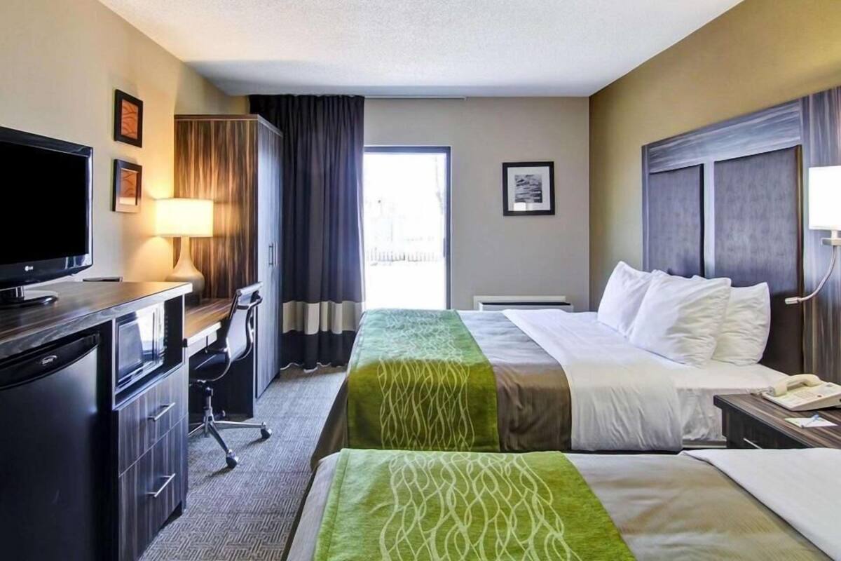 Una habitación de hotel con cama, escritorio, televisión, lámpara y ventana con cortinas.