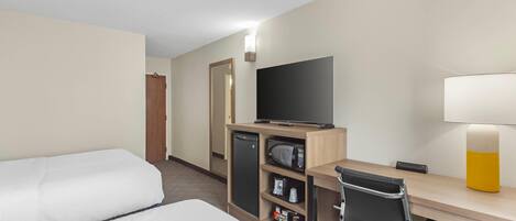 A hotel room with two beds, a desk with a computer, a television, a microwave, and a small refrigerator.