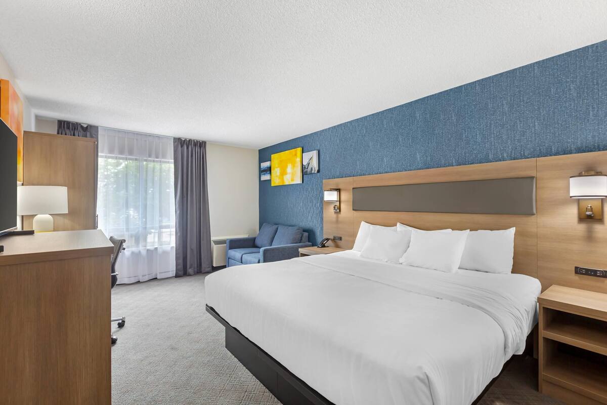 Habitación de hotel con una cama grande, un escritorio, una silla, un televisor y una ventana con cortinas.