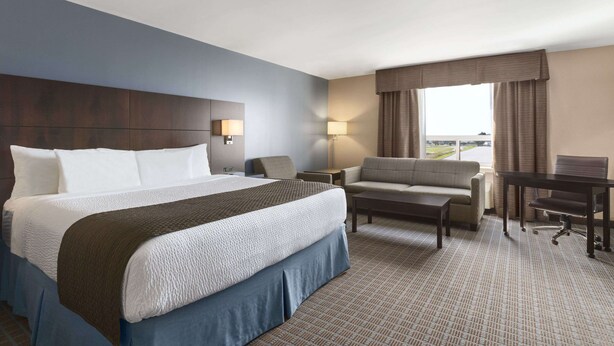 A hotel room with a large bed, a desk, a chair, and a sofa. - Days Inn by Wyndham Stephenville (Stephenville)