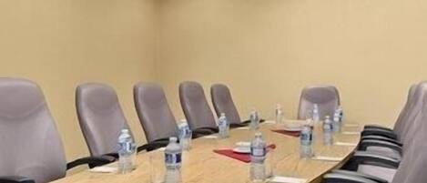 Un salón de conferencias con una larga mesa, múltiples sillas y botellas de agua sobre la mesa.