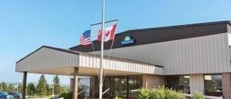 A modern hotel with a covered entrance, American and Canadian flags, and a parking lot.