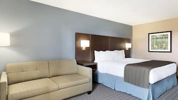 Una habitación de hotel con una cama, un sofá, una mesita de noche y una lámpara de pared.