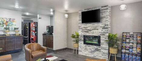 A modern lobby with leather sofas, a stone wall with a TV, a coffee machine, and a plant stand.