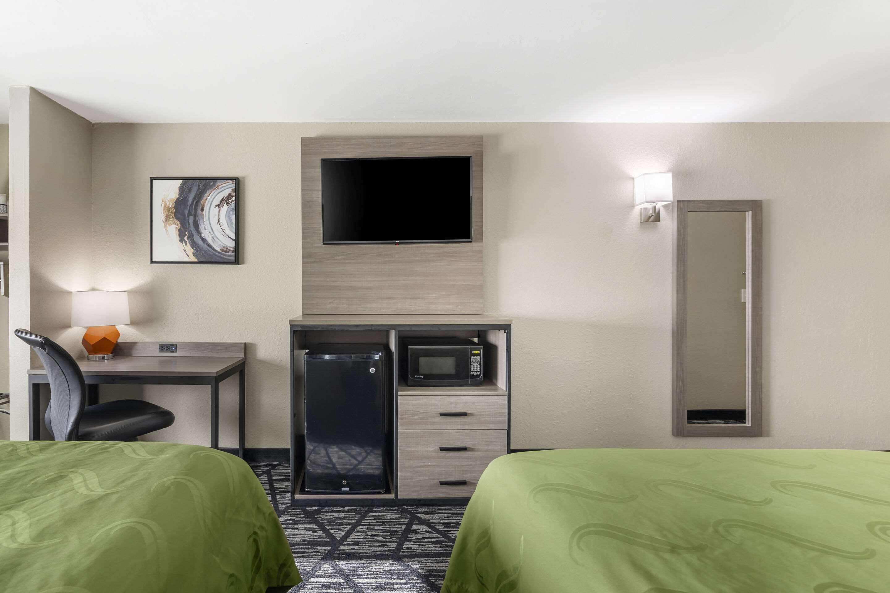 A hotel room with two beds, a desk with a microwave, a TV, and a mirror.