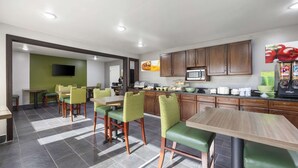A modern restaurant with green chairs, a kitchen area, and a flat-screen TV mounted on the wall. - Quality Inn Jackson Northwest (Jackson)