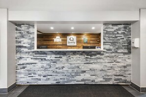 A reception area with a modern design, featuring a marble-patterned wall, a wooden accent wall, and a sign that reads "Quality by Choice Hotels."