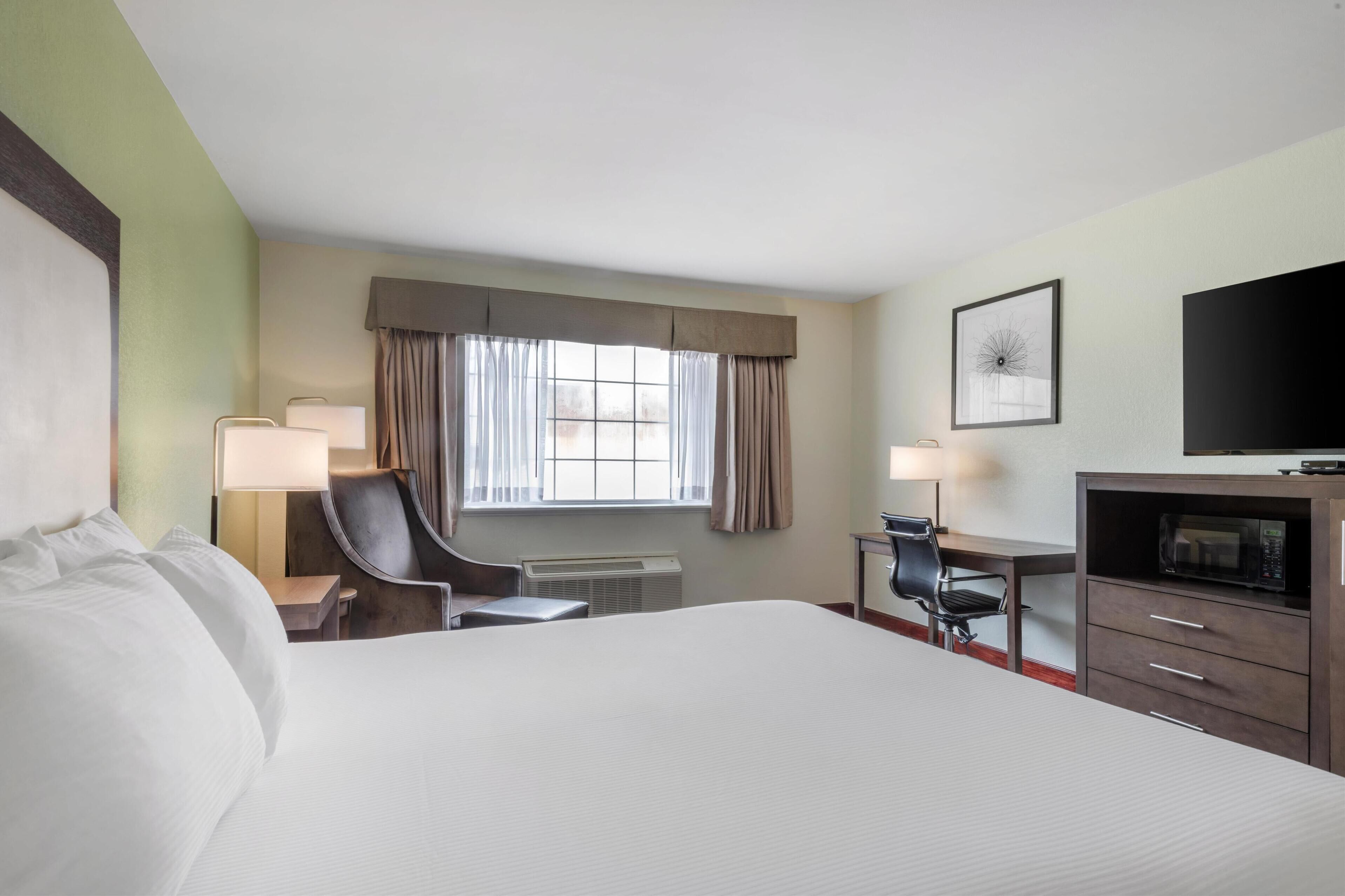 A hotel room with a large bed, a desk with a chair, a television, and a window with curtains.