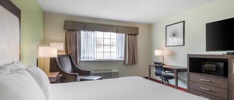 A hotel room with a large bed, a desk with a chair, a television, and a window with curtains.