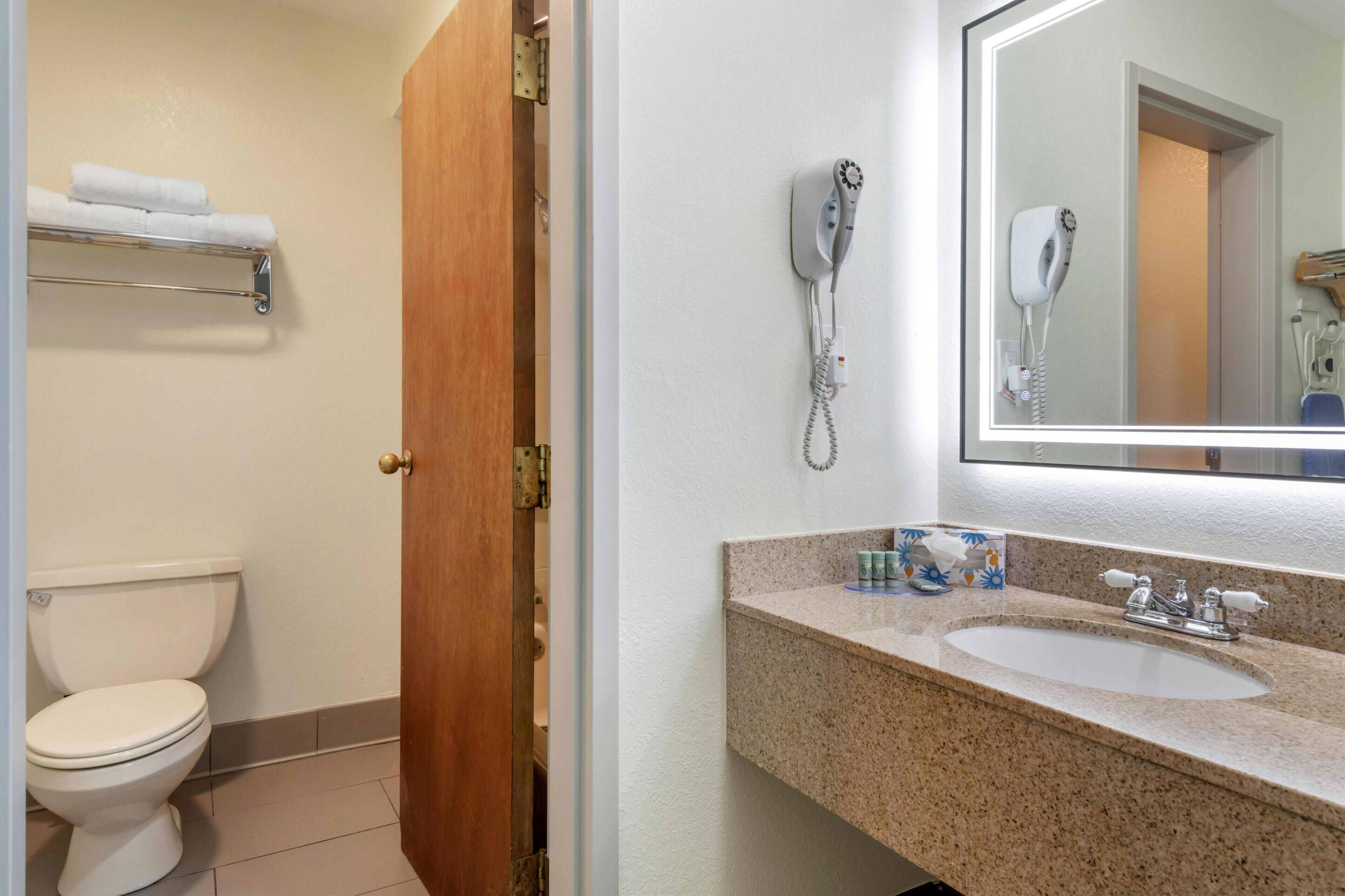 Un baño con inodoro, lavamanos, secador de pelo y toallero.