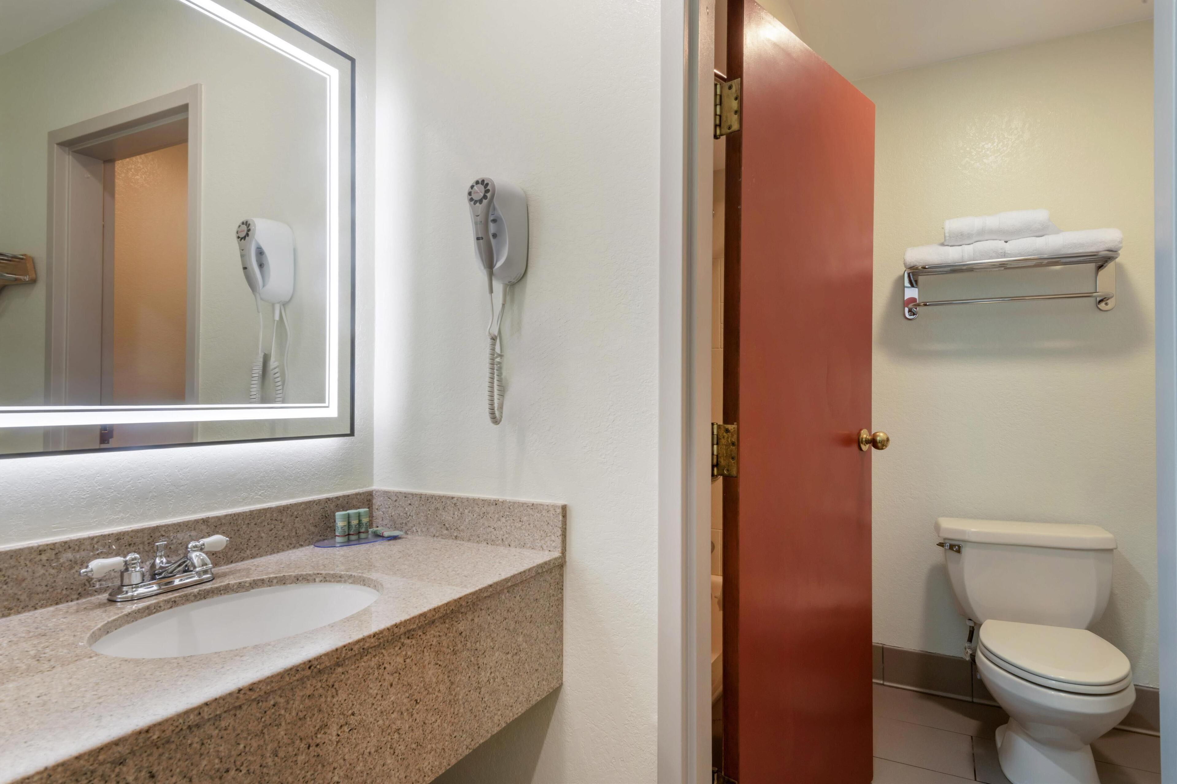 Une salle de bain équipée d’un lavabo, d’un miroir, d’un sèche-cheveux et de toilettes.