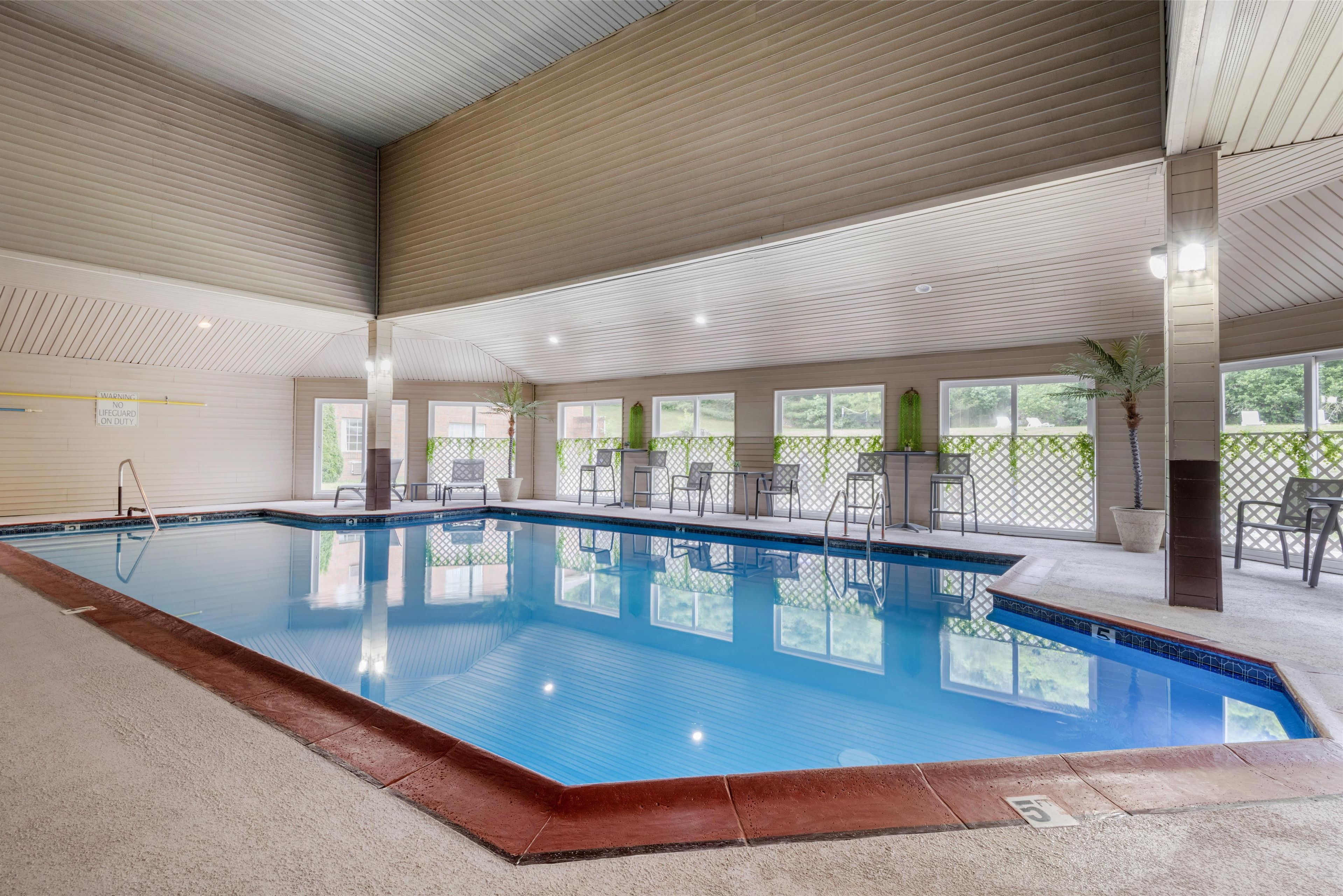 Ein überdachter Pool mit klarem Wasser, umgeben von Stühlen und Tischen, mit großen Fenstern für natürliches Licht.