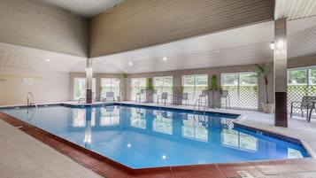 Ein überdachter Pool mit klarem Wasser, umgeben von Stühlen und Tischen, mit großen Fenstern für natürliches Licht.