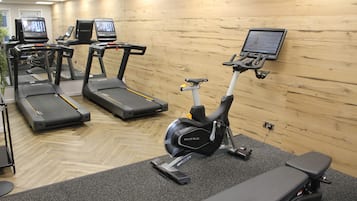 A gym with treadmills, an elliptical, and a stationary bike, equipped with screens and a bench.