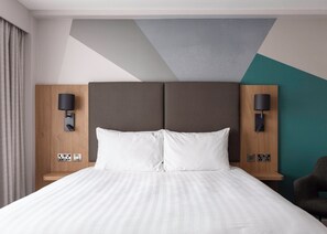 A modern hotel room with a large bed, two bedside tables with lamps, and a geometric-patterned ceiling.