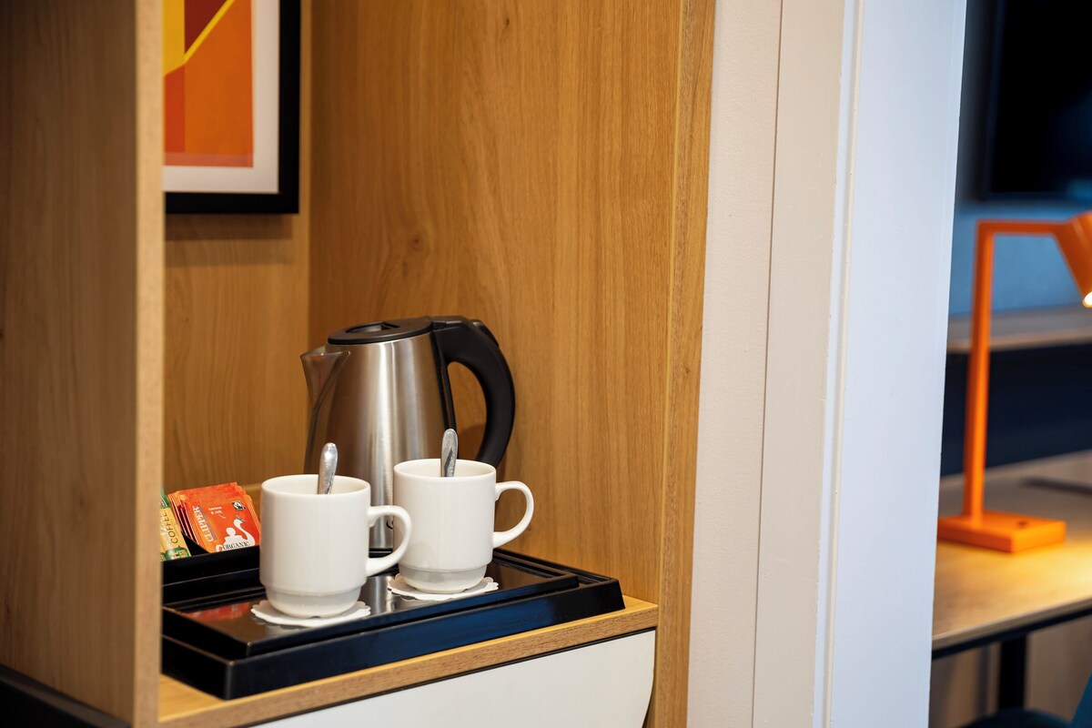A coffee station with a kettle, two white cups, and a packet of coffee.