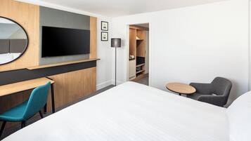 Une chambre d’hôtel avec un grand lit, un bureau avec une chaise, une télévision et une petite table avec une chaise.