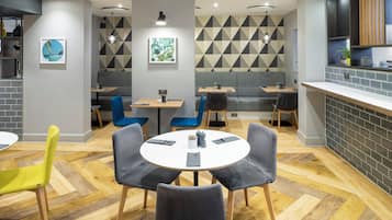 A modern restaurant with round tables, grey and blue chairs, and a geometric patterned wall.