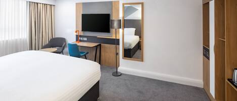 A hotel room with a large bed, a desk with a chair, a television, and a mirror.