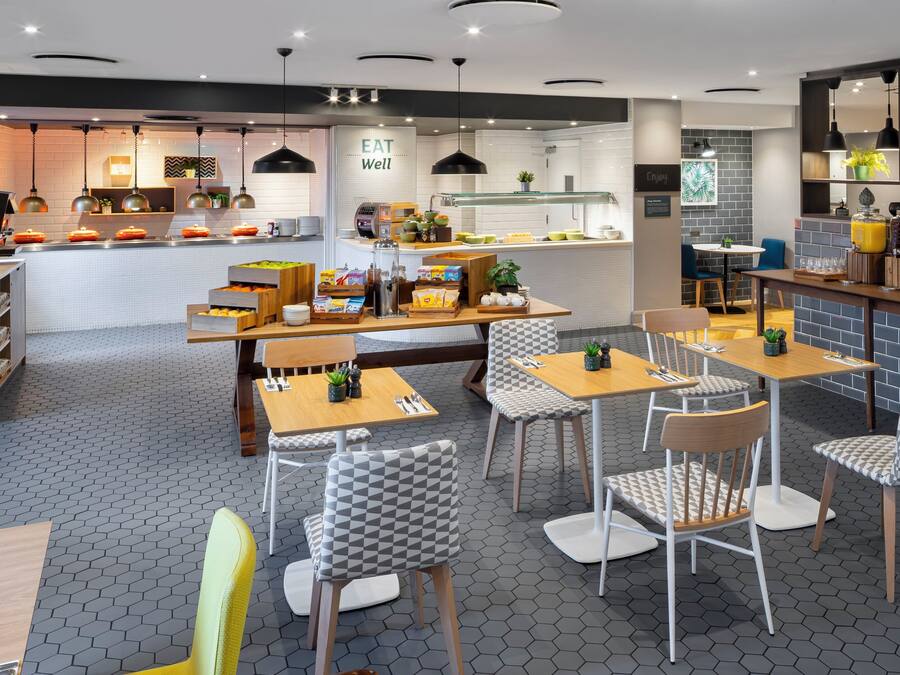 Un café moderno con suelo de baldosas hexagonales, mesas y sillas de madera, y una barra central con productos alimenticios.