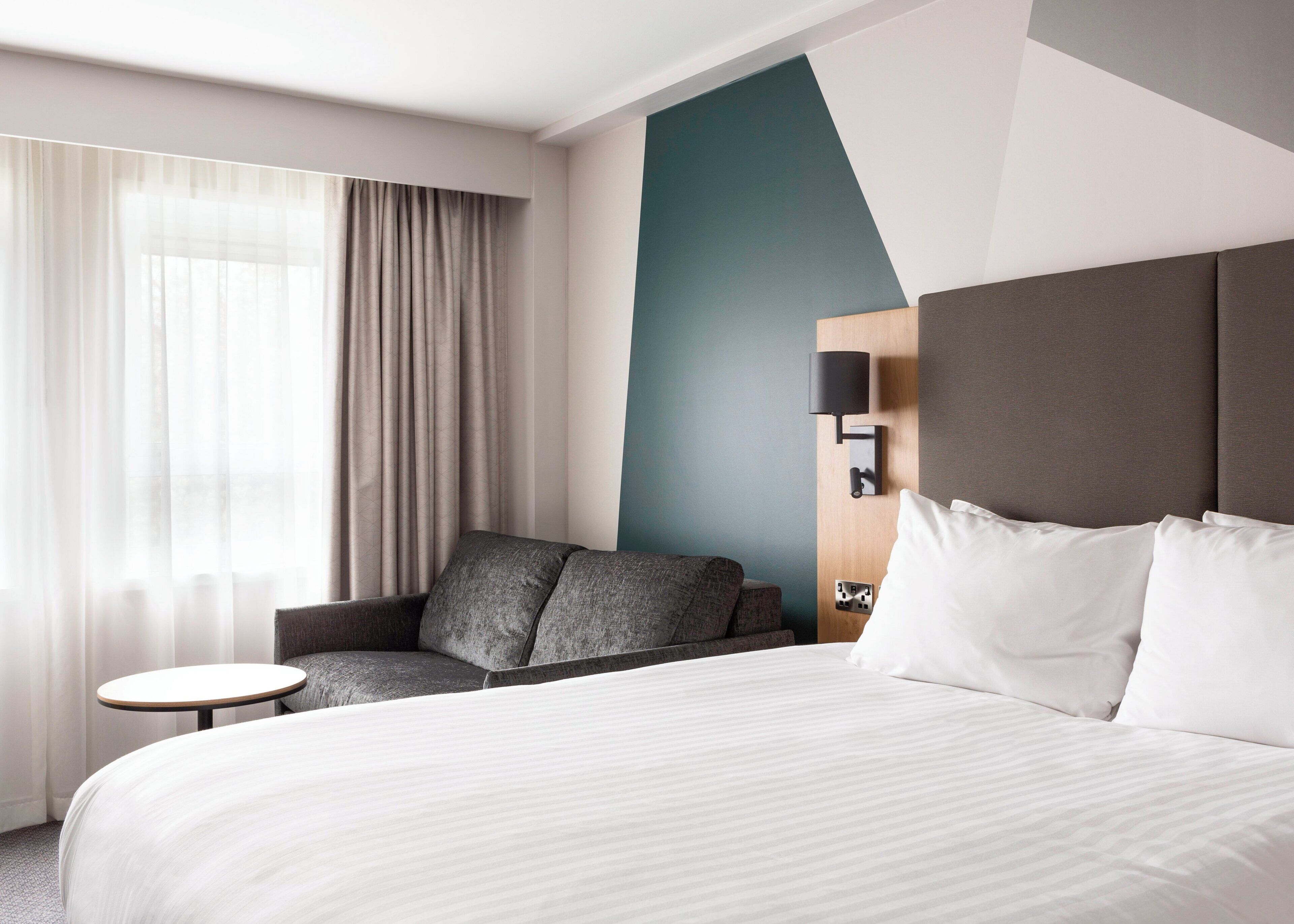 Une chambre d’hôtel avec un lit, un canapé, une petite table et une lampe fixée au mur.