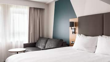 Une chambre d’hôtel avec un lit, un canapé, une petite table et une lampe fixée au mur.