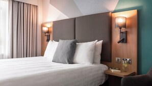 A hotel room with a large bed, two wall-mounted lamps, a nightstand with a glass, and a chair. - Holiday Inn London-Bexley by IHG (Bexley)