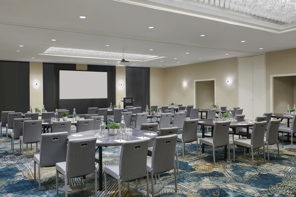 A conference room with round tables, grey chairs, and a large screen.