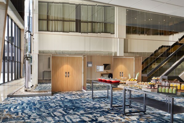 A modern hotel lobby with a spacious atrium, a staircase, and a buffet area with various food and drink options. - Delta Hotels by Marriott Calgary Airport In-Terminal (Calgary)